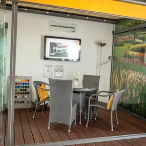Moderner Terrassenüberdachung-Showroom mit Sitzgruppe, Farbmustern und Blumenmotiv.