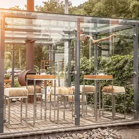 Moderne Außenterrasse mit Glasüberdachung, Holzbarhockern und gemütlicher Atmosphäre.