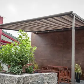 Moderne Terrassenüberdachung mit Markise, Sitzbank und Pflanzen im Gartenbereich.