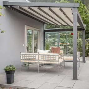 Moderne Terrassenüberdachung aus Aluminium mit gemütlicher Sitzgruppe und Glaswand.
