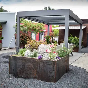 Moderner Garten mit Hochbeet aus Cortenstahl, Blumen und überdachter Terrasse.