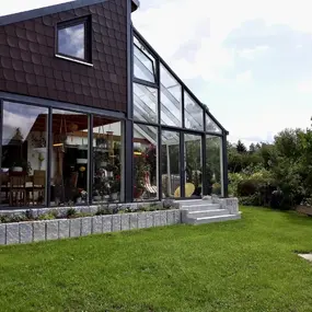 Modernes Wohnhaus mit großem Wintergarten und gepflegtem Garten im Grünen.